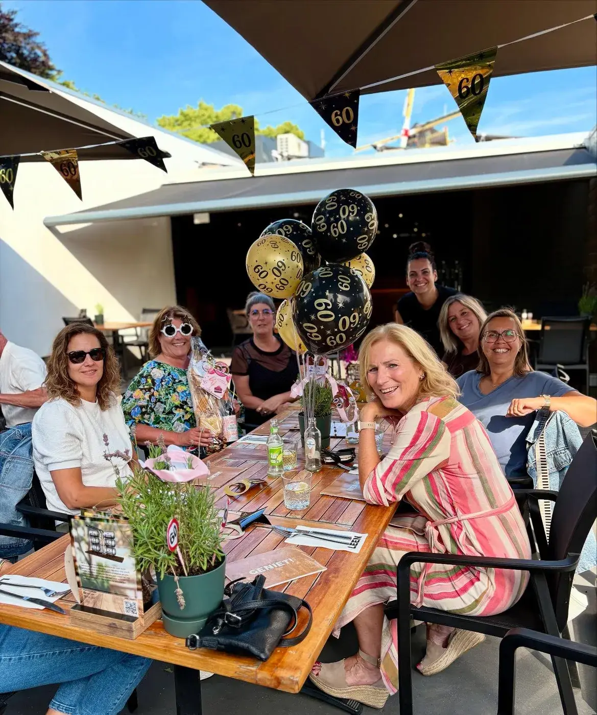 Groep gasten viert een verjaardag met ballonnen aan een lange tafel op het terras van Club LEEN