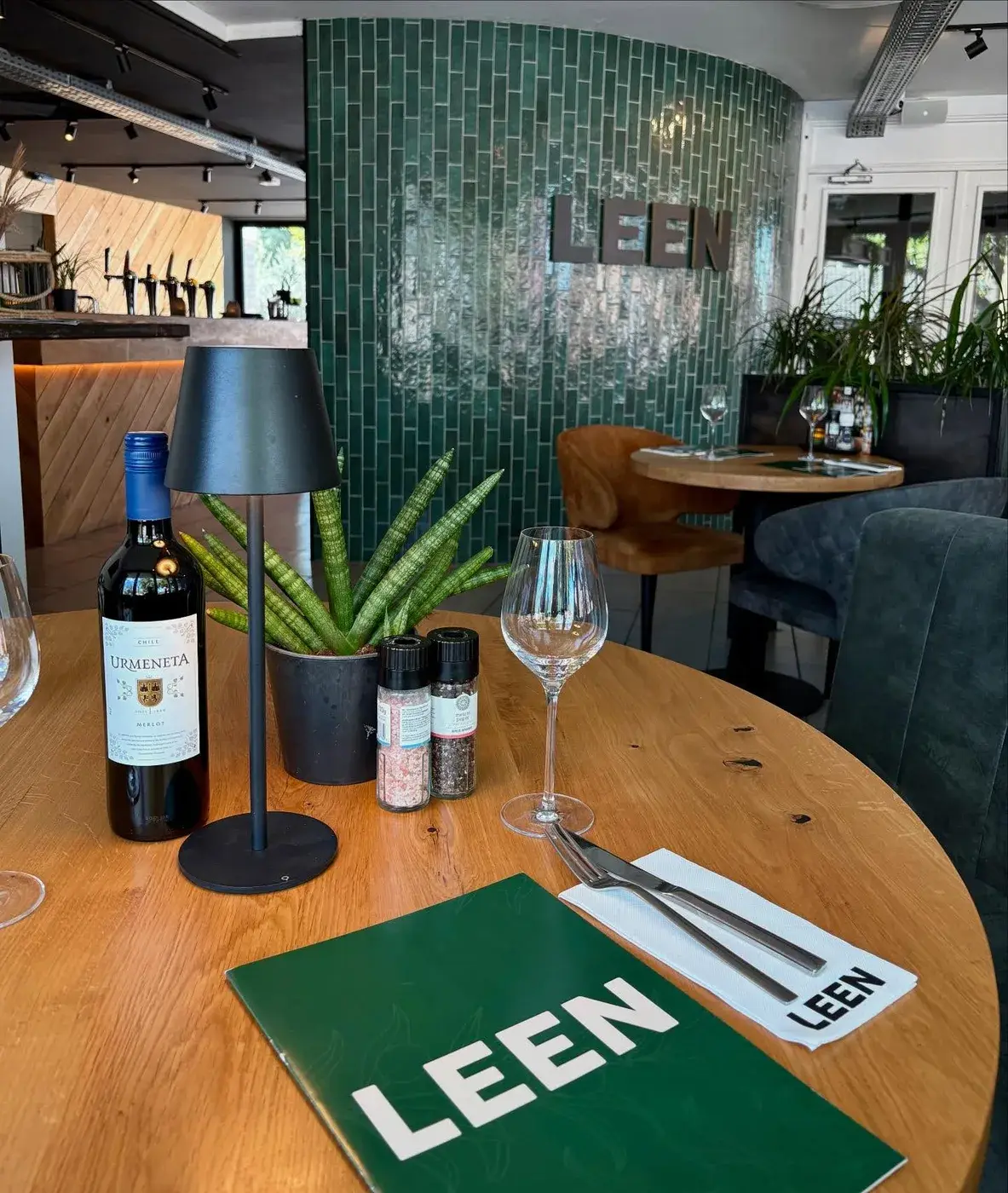 Sfeervol interieur van Club LEEN met groene wandtegels, houten tafel en menukaart