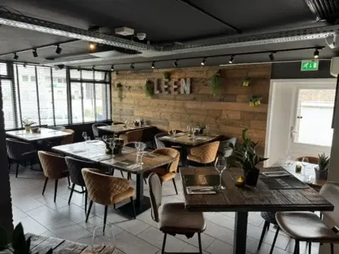Overzicht van De Eetkamer van Club LEEN met gedekte houten tafels en comfortabele stoelen