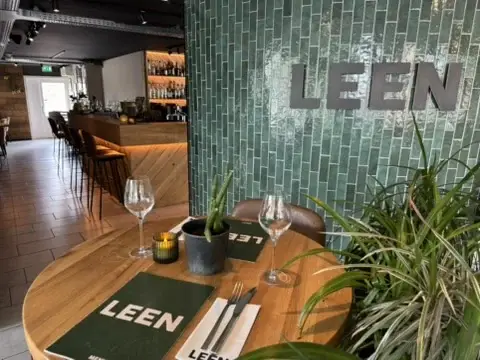 De Lounge van Club LEEN met groene LEEN-tegelwand, gedekte tafel en bar op de achtergrond