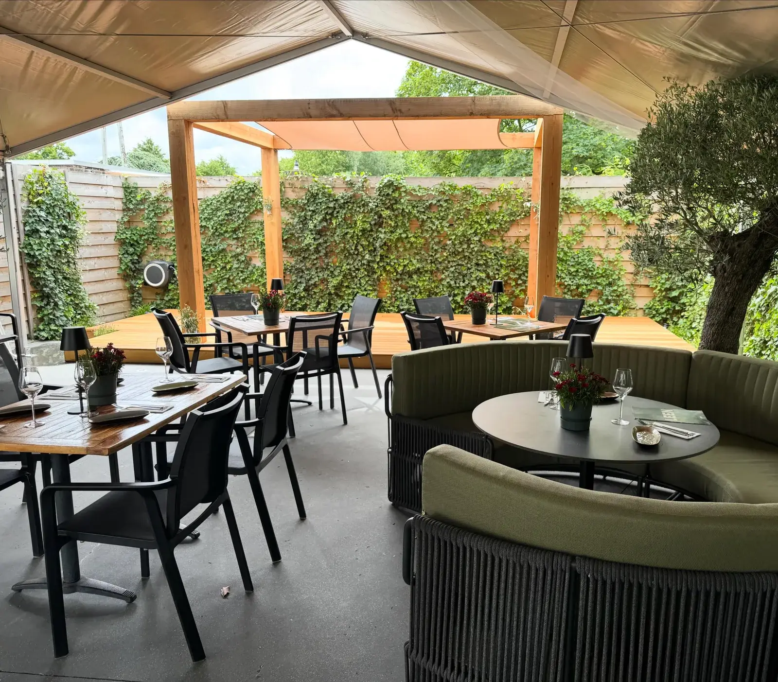 Overdekt terras van Club LEEN met loungebanken, pergola en groene haag