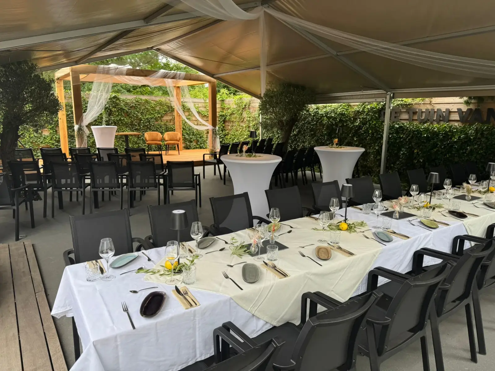 Overdekt terras van Club LEEN in feestopstelling met gedekte tafels, statafels en podium in De Tuin van LEEN